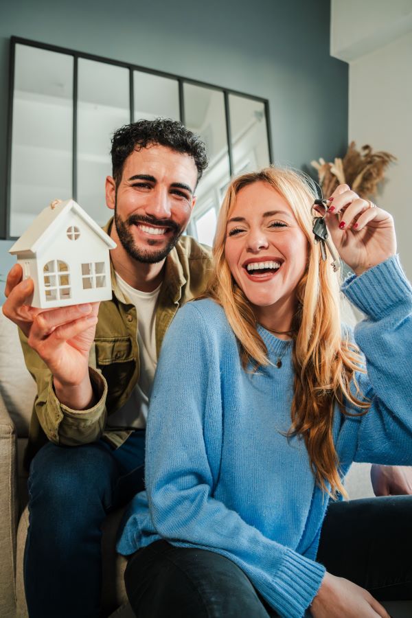 couple celebrating a beginning at their new home holding the key of the house. Happy property owners at living room.